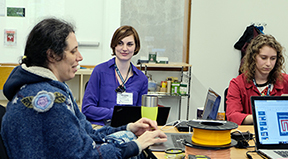 A faculty member with a disability types on a computer while students work in the background. A faculty member with a disability types on a computer while students work in the background.