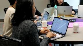 A woman works on a computer at a table with others. A woman works on a computer at a table with others.