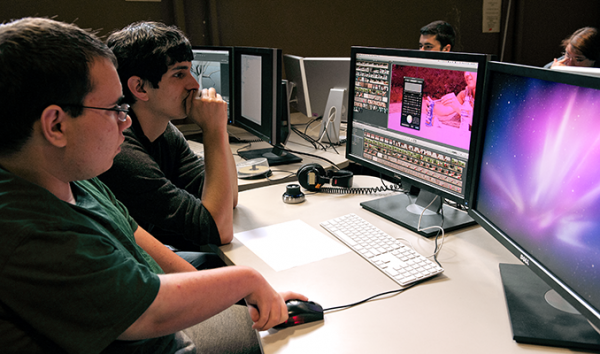 A student with a disability works with an educator to edit a video on a desktop computer