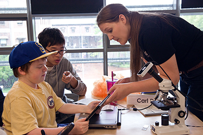 An instructor helps two students on a tablet.